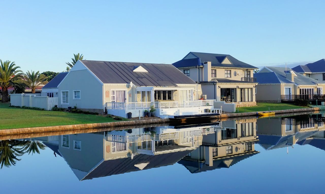 services-03 Luxury modern homes reflecting on a peaceful, clear lake during daylight, showcasing architectural beauty.